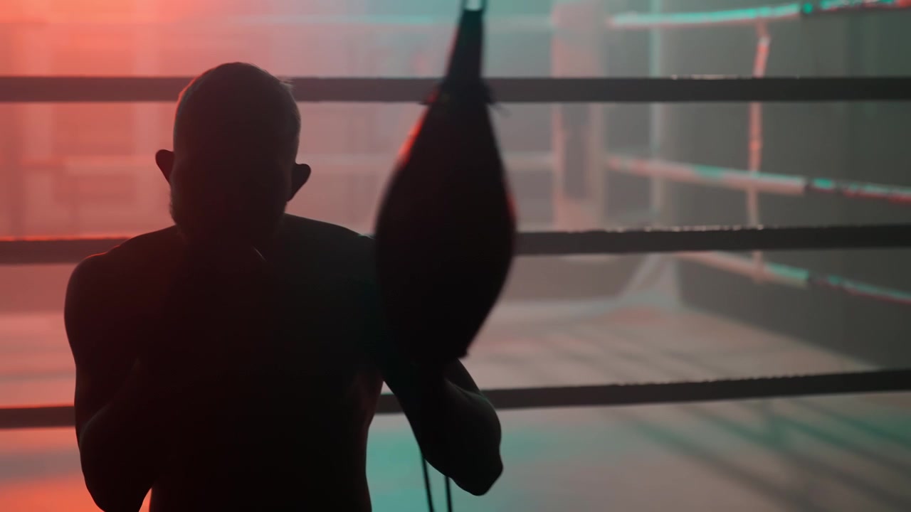 Sagoma di un pugile uomo che si allena con un punching ball in un ring da boxe buio