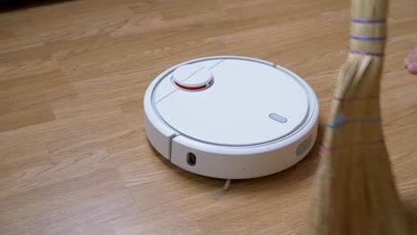 robot vacuum sweeps debris on floor against background of a sweeping broom. 4k