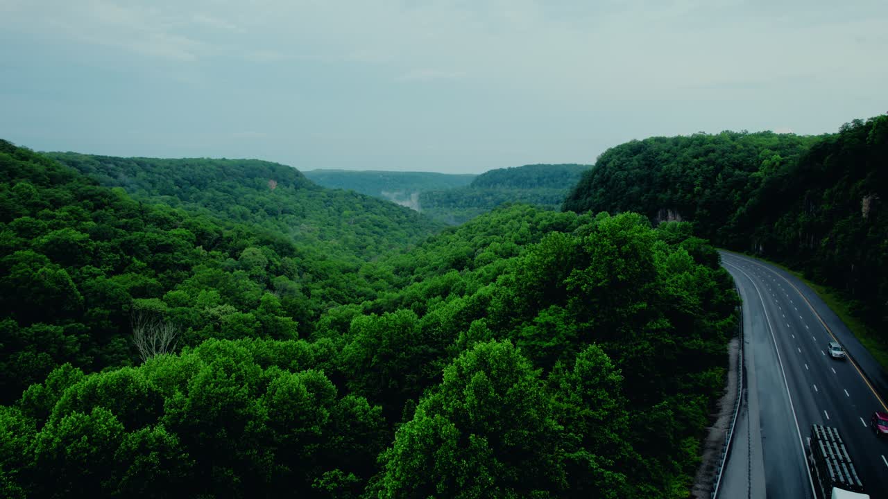 Semi truck on I-24 crossing Monteagle Pass in Tennessee, surrounded by forested hills and cloudy skies.
