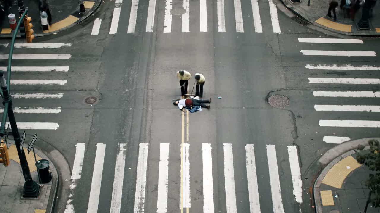 Two workers in yellow vests direct traffic in a busy downtown intersection. Cars pass by as they help maintain safety and order on the road. The scene captures urban life in action.