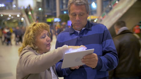 Pareja-Mayor-Teniendo-Una-Conversación-Vívida-Usando-Pad-En-El-Aeropuerto