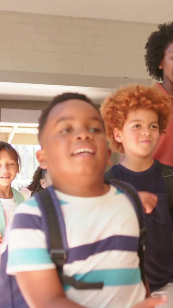 Vertical video: Running through doorway boy in striped tee backpack entering porch heading to class