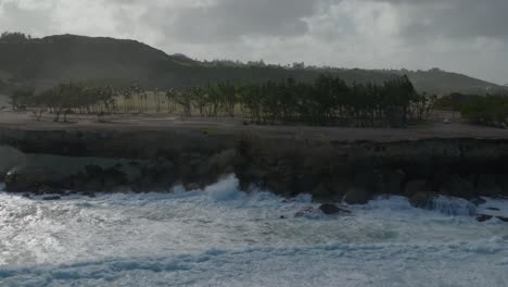 drone dolly por encima de las olas del océano chocando contra la costa rocosa con cocoteros en el borde del acantilado
