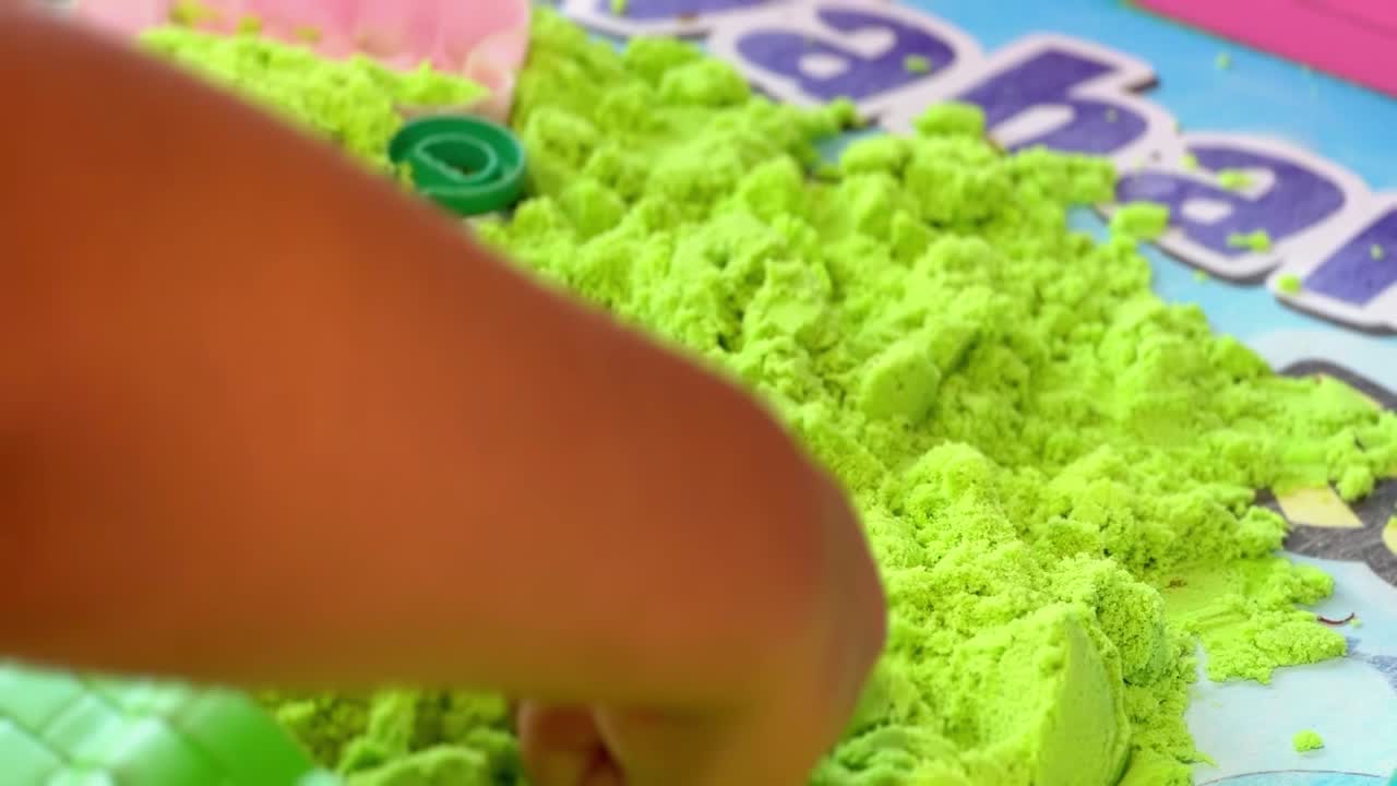 Mãos de criança brincando com areia colorida.
