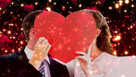 recién casados con un gran corazón rojo frente a sus caras