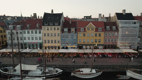 a picturesque sunset over nyhavn, copenhagen, setting a cozy mood with lively crowds and boats sailing along the canal