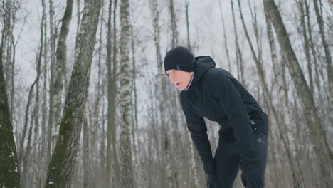 a young man on a morning jog in the winter forest was tired and stopped to catch his breath. he recovered his strength and overcame fatigue and continued to run. perseverance and overcoming weakness. push forward