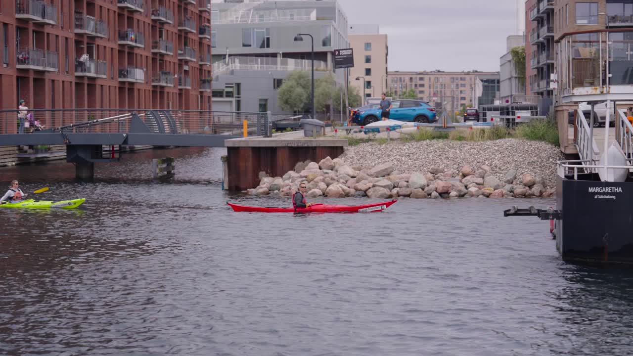 People use single seat canoe and paddle in river with urban background, Denmark