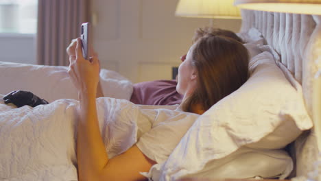 couple with woman with prosthetic arm in bed looking at mobile phone together