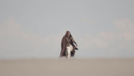 a lone, robed character battles against strong wind and haze while walking through a barren landscape. a cinematic concept of struggle, perseverance, and a difficult journey