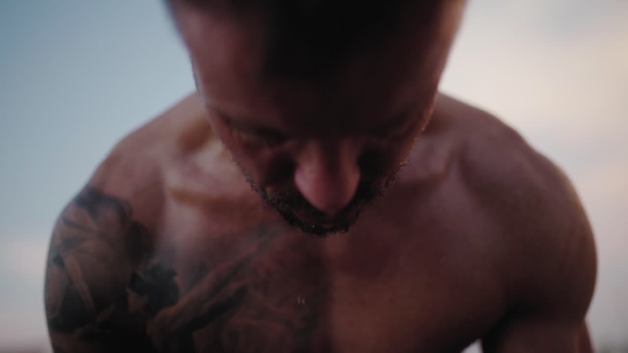 지친 남자 선수의 얼굴에서 물이 떨어지고, 외부 체육관에서 운동을 한다