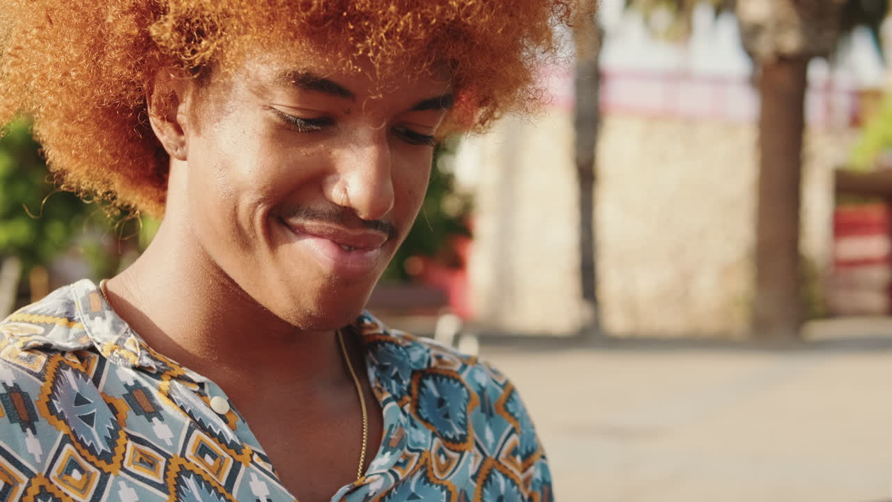 Young Man with Curly Ginger Hair Using Smartphone Outdoors