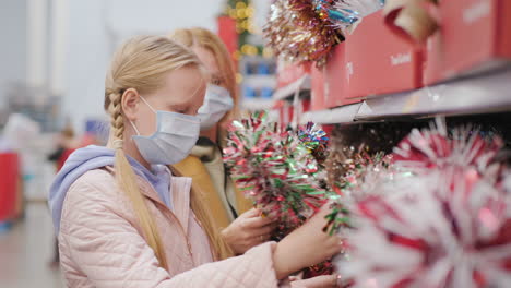 Mom-and-daughter-choose-decorations-for-the-Christmas-tree-in-the-store.-Wear-protective-masks