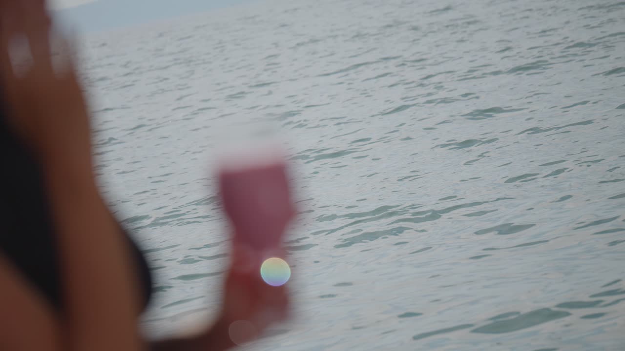 A young woman holding a smoothie strawberry milkshake while standing outdoors near the wavy lakeside in soft sunlight