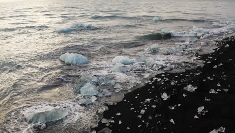 tiro estático en cámara lenta de olas rompiendo contra cubos de hielo derritiéndose en la playa de diamante negro en la isla de islandia