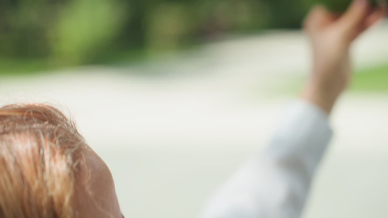 Madre al aire libre examinando una hoja verde, sonriendo suavemente, luz del sol en la cara, primer plano de perfil, brisa suave, fondo de parque, estado de ánimo contemplativo, conexión con la naturaleza, toma espontánea de estilo de vida ideal para el bienestar.