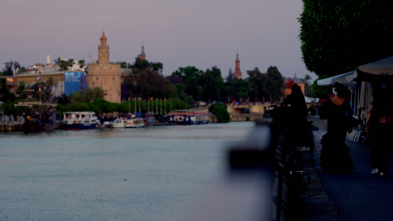 Wide view of Seville's riverside promenade during golden hour with casual strollers