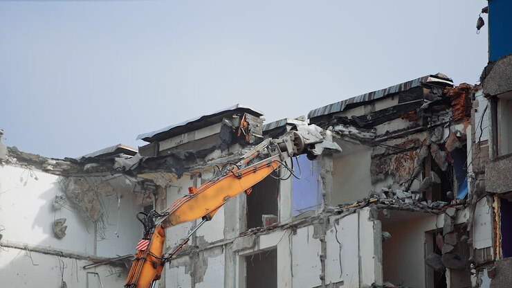 Macchina speciale che demolisce una casa in cemento. Escavatore con frantumatori idraulici durante la demolizione della casa.
