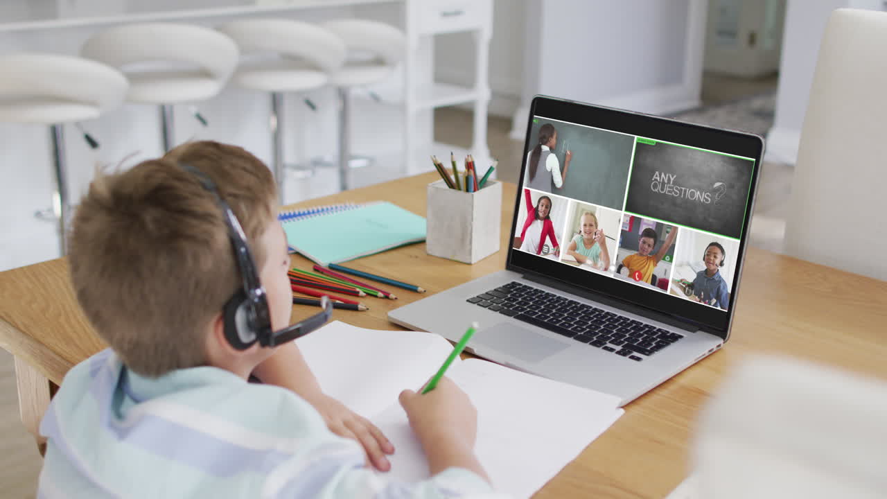 Schoolboy using laptop for online lesson at home, with diverse teacher and class on screen