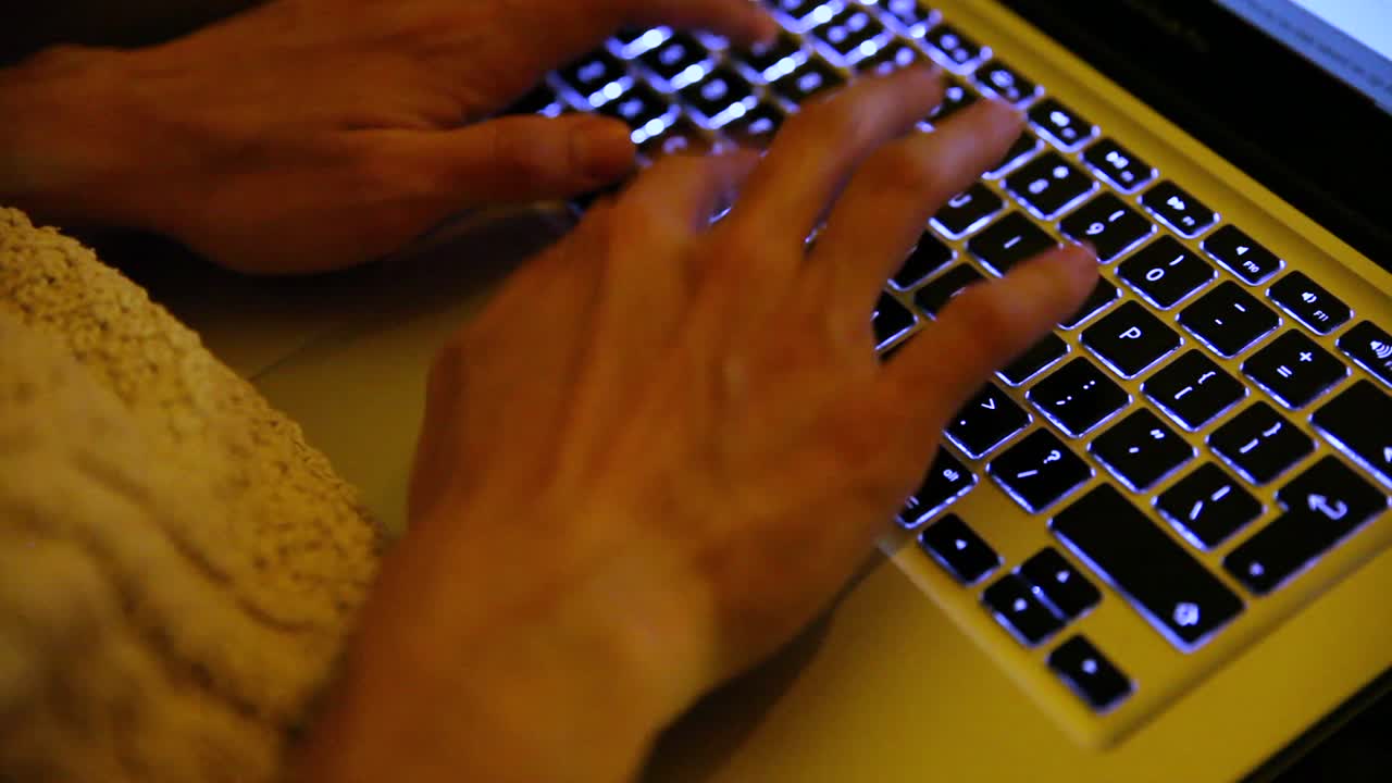 Cinematic blurred hands typing on a lighted laptop keyboard