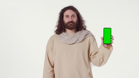 portrait of man wearing robes with long hair and beard representing figure of jesus christ holding green screen mobile phone