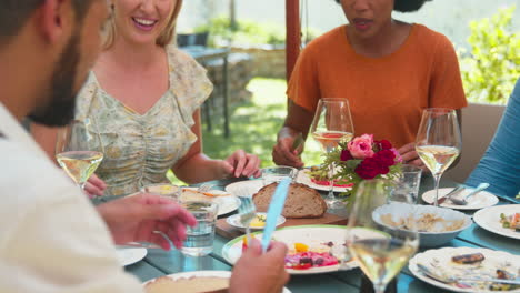 group of friends enjoying outdoor meal and wine on visit to vineyard restaurant