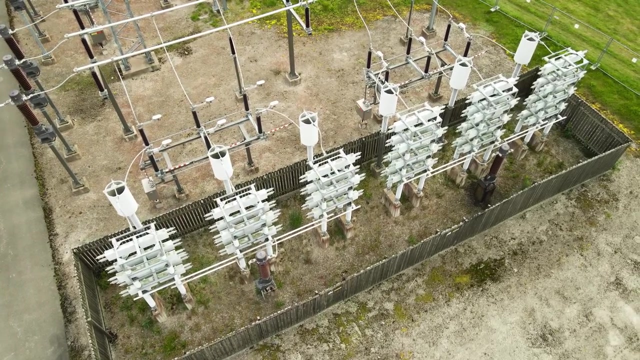 Luftaufnahme eines modernen Hochspannungs-Umspannwerks, das das komplexe Netzwerk aus Stromleitungen, Keramikisolatoren und Verteiltransformatoren zur Steuerung des Energieflusses im Stromnetz zeigt.