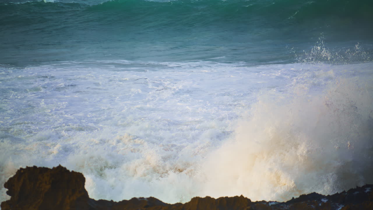 las olas blancas del mar golpean las rocas de la playa en cámara lenta. espumando el océano tormentoso rodando
