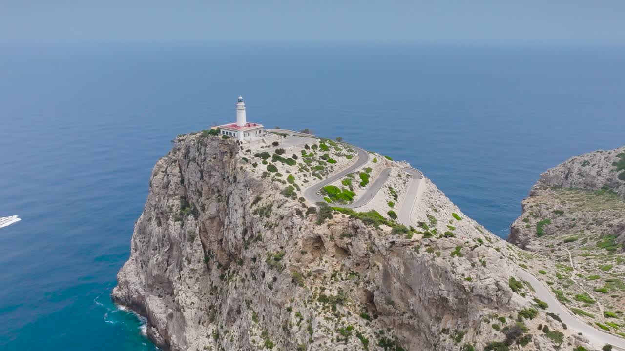 Veduta con drone di una barca nel mare dalle acque blu vicino a un faro su una scogliera, Maiorca