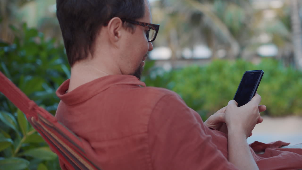 hombre usando un teléfono inteligente en una hamaca