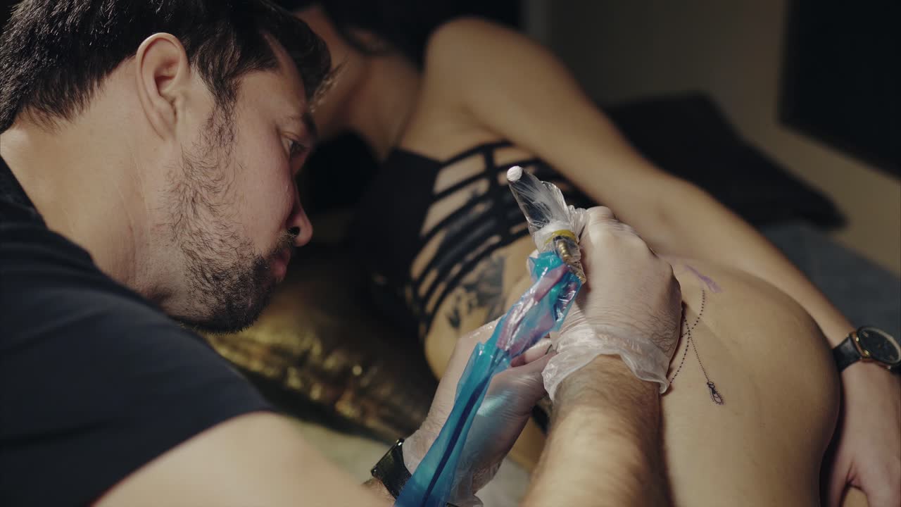 artista del tatuaje trabajando en el trasero de una mujer