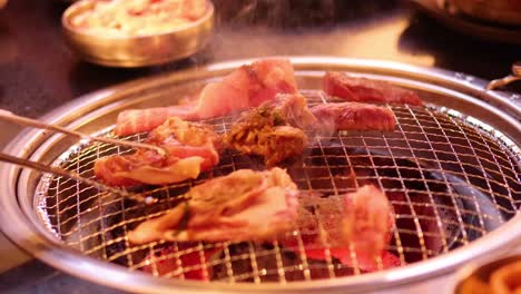 tongs flipping meat on a barbecue grill