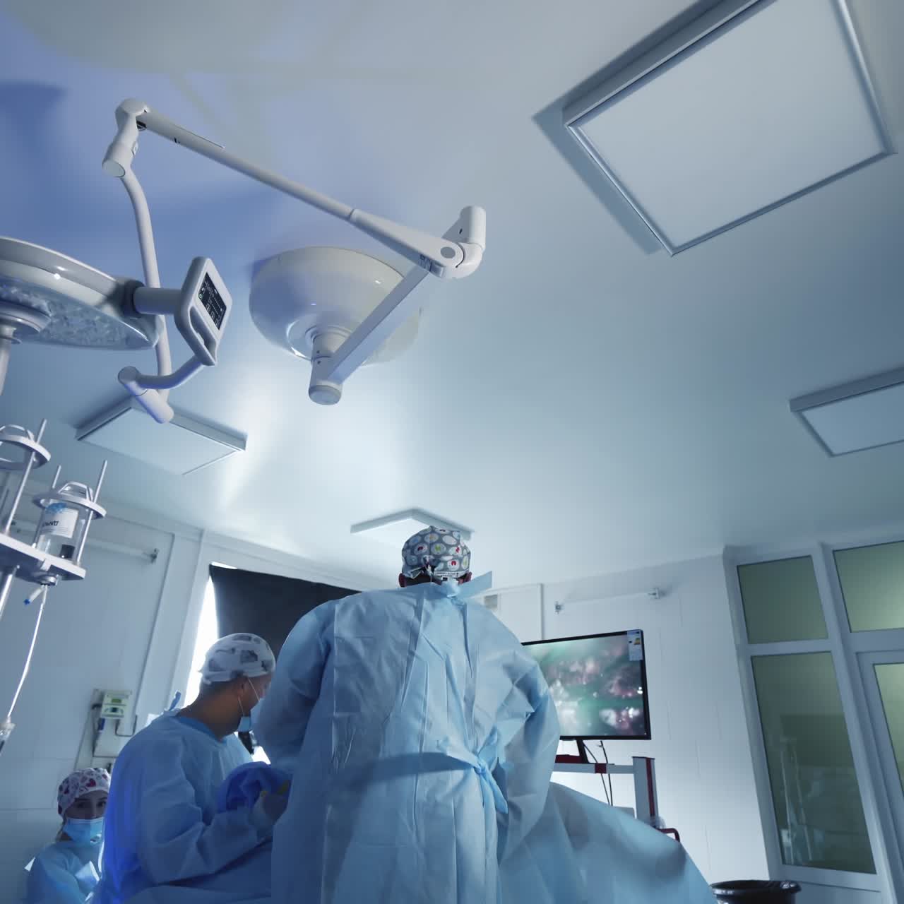 Modern operating theater. Doctors use computer technologies during the surgery. Back view of surgeons conducting an operation and looking on monitor.