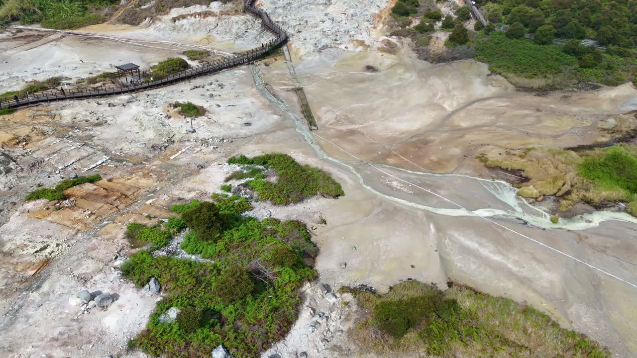 Drone view of the active geothermal area of Sikidang Crater in Dieng, with boiling steam, sulfur rocks, and scenic mountain surroundings