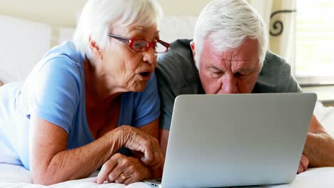 couple lying on bed and using laptop