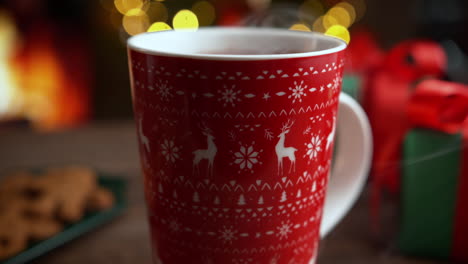 hot cocoa in a red mug with a christmas reindeer pattern by the fireplace
