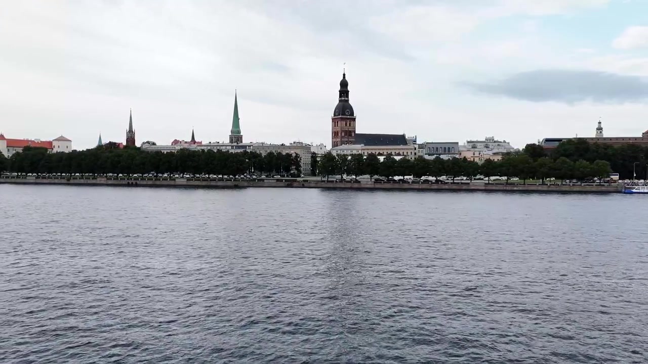 Lo skyline della Città Vecchia di Riga con la Cattedrale di Riga e le guglie delle chiese si erge dietro gli alberi lungo il lungofiume del Daugava, visto dall'altra sponda.