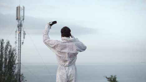 man in protection suit standing on the edge of the roof put off the respirator, rear view