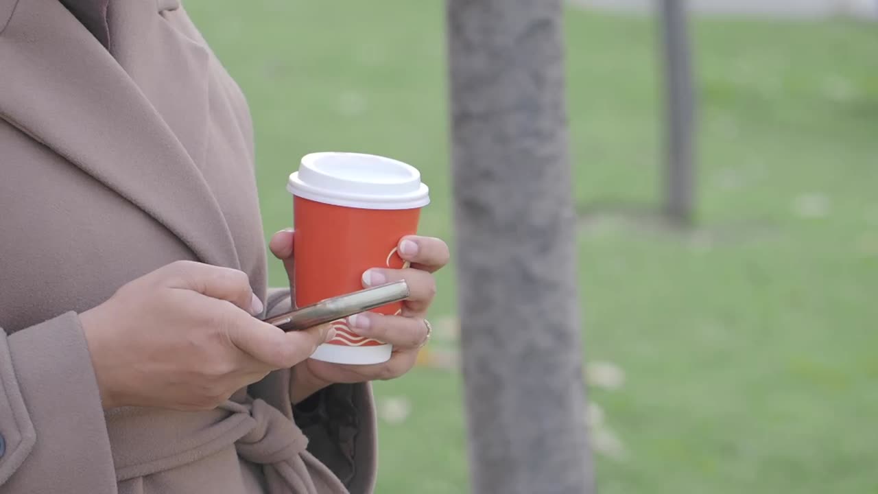 Person, die Kaffeetasse und Smartphone im Freien hält