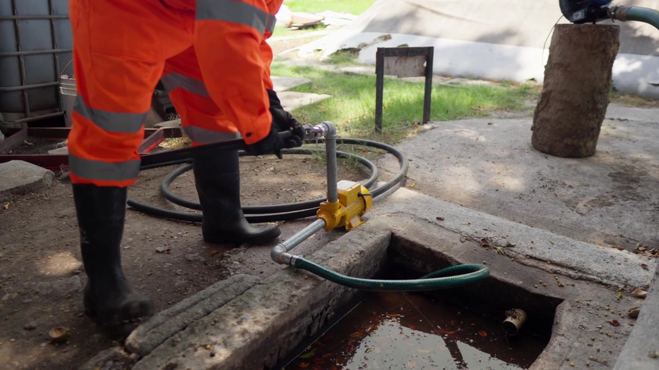 En ugjenkjennelig arbeider i kjeledress kobler en slange til en hydropumpe for å pumpe ut vann blandet med organiske rester fra en grop, som en del av et sirkulært landbruksinitiativ