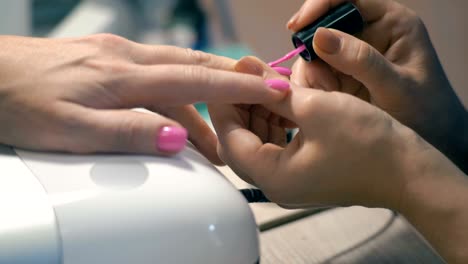 close-up, master of manicure: applying pink lacquer on nails on woman's hand