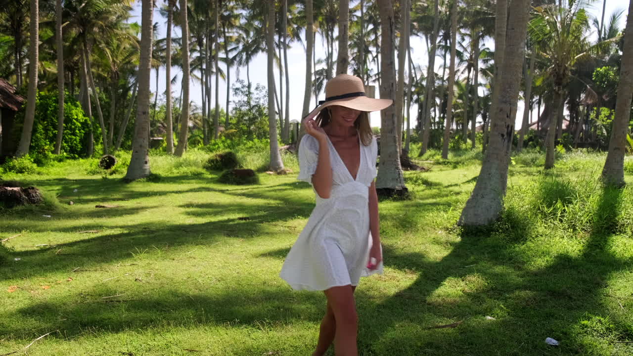 Mujer con sombrero de paja caminando por un palmeral tropical