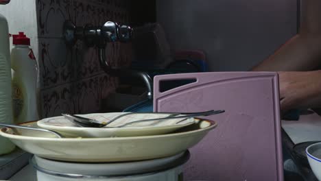 man washing up in kitchen sink with dirty dishes stacked on worktop