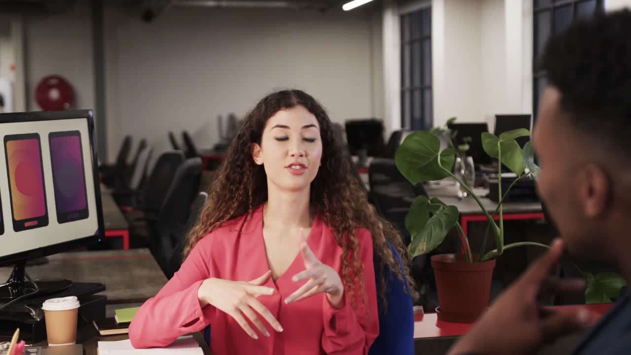 Dois colegas criativos diversos e felizes em discussão ao computador em escritório casual, em câmara lenta.