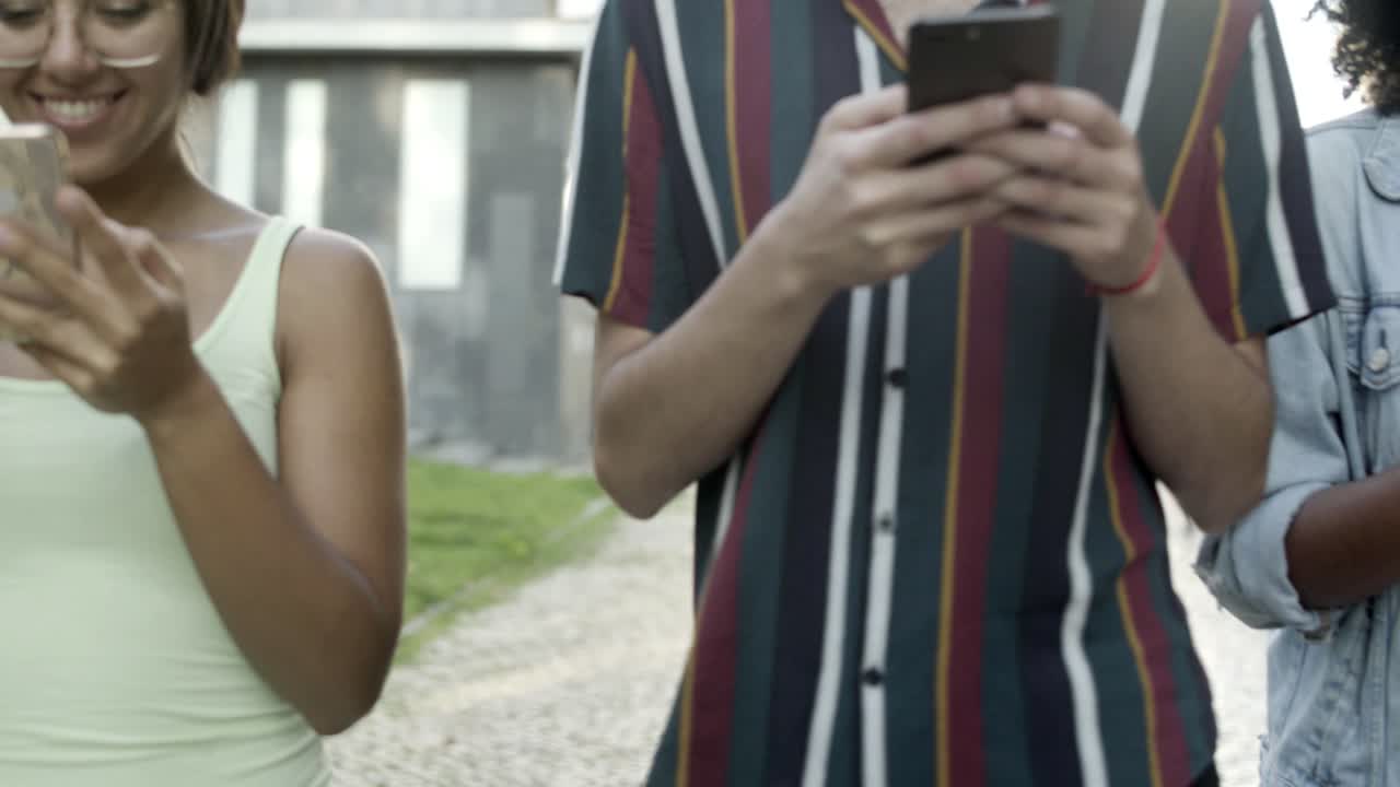 amigos sonrientes con teléfonos inteligentes en el callejón del parque