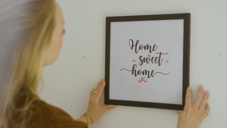 woman hanging up "home sweet home" frame on wall