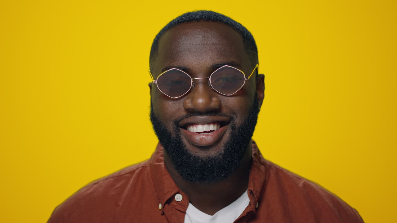 retrato de un hombre afroamericano sonriendo a la cámara sobre un fondo amarillo.