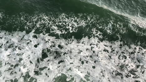 Aerial-bird-eye-view-panning-shot-flying-over-sea-foam-and-waves