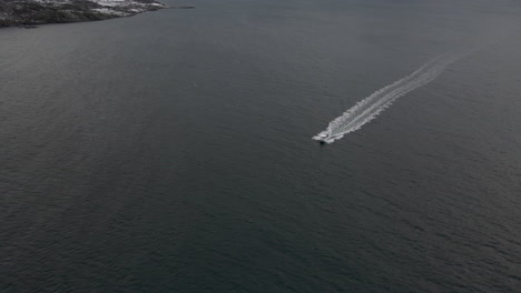 Drone-tracking-boat-cruising-along-Arctic-waters,-high-angle-view