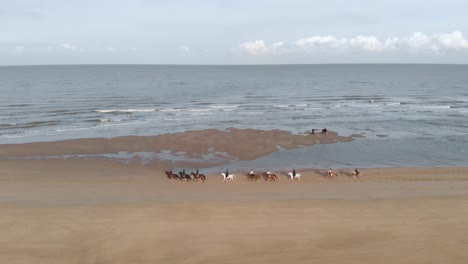 Aerial-View-Of-People-Horseback-Riding-At-The-Beach-In-Netherlands